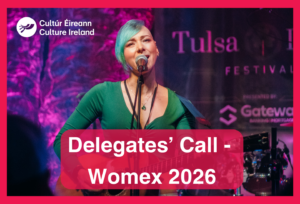 A woman sings into a microphone while playing a guitar on stage. Text reads - Delegates' Call Womex 2026.